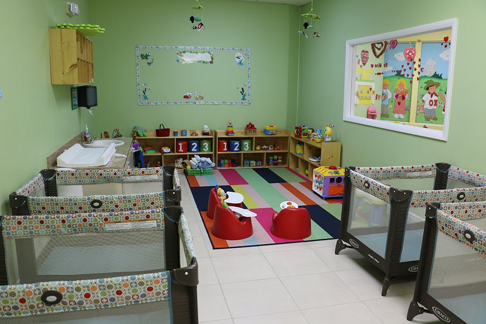 Nursery room with cribs, changing table, colorful rug, and toys