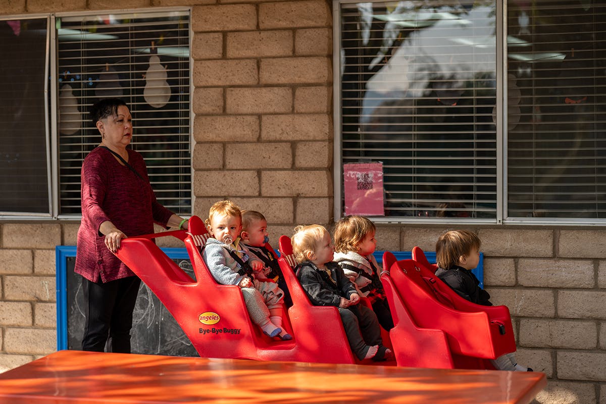 Person pushing multiple children in a red multi-seat stroller