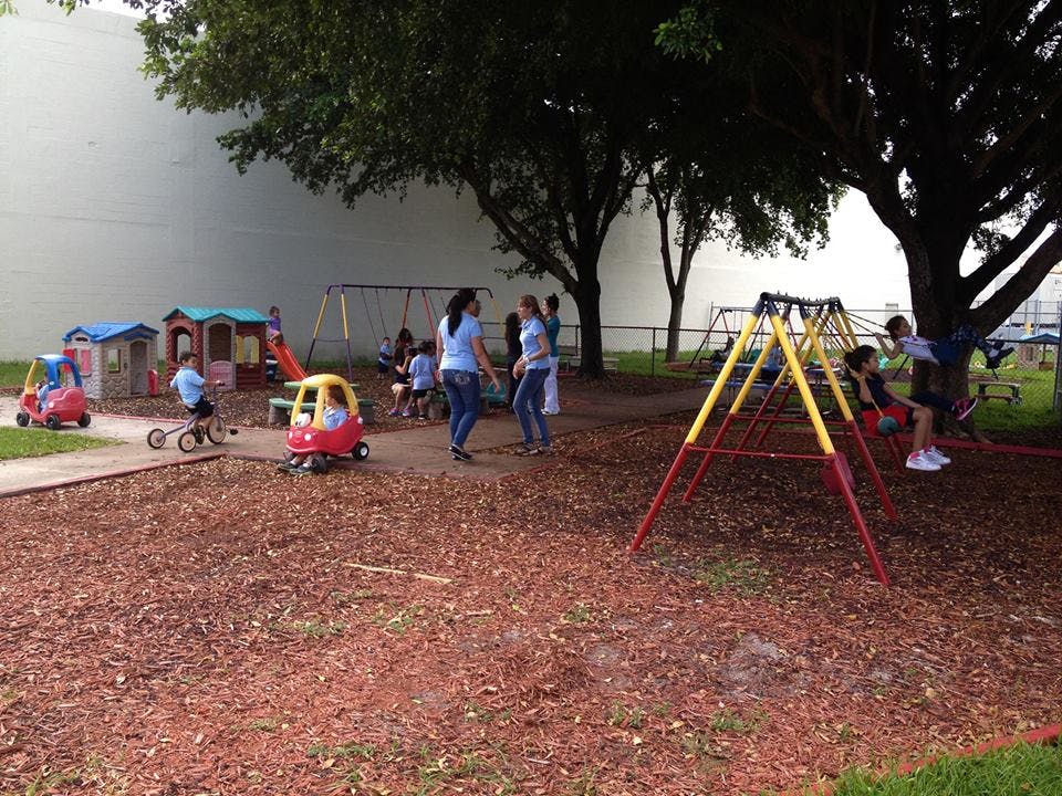 People and children on a playground with play structures and wood chips