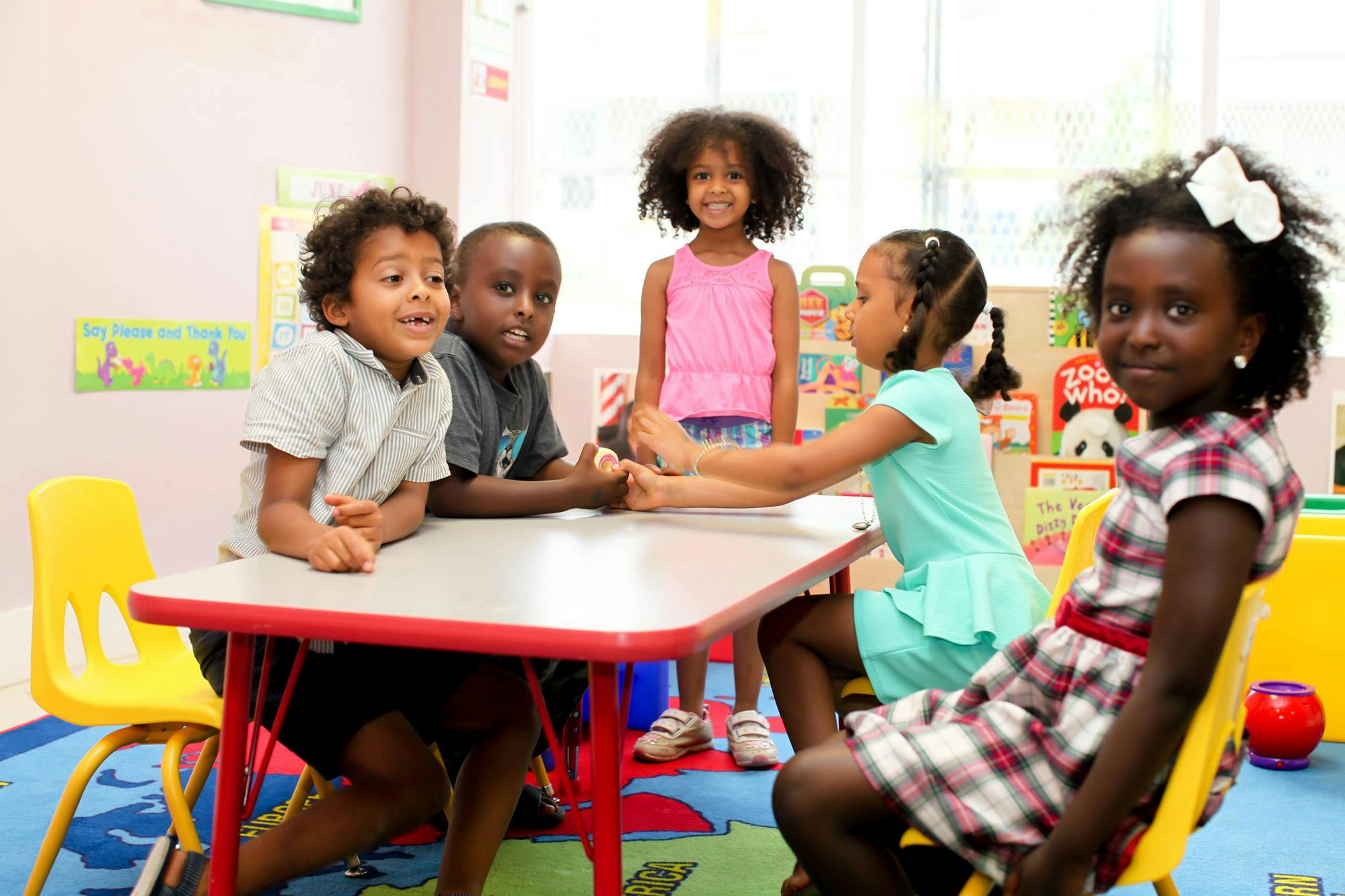 Children sitting and standing around a table in a classroom