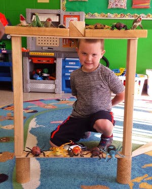 Child crouching under a wooden frame with toy insects on the floor