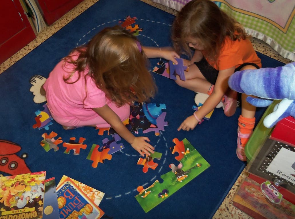 Two children playing with a puzzle on a blue rug