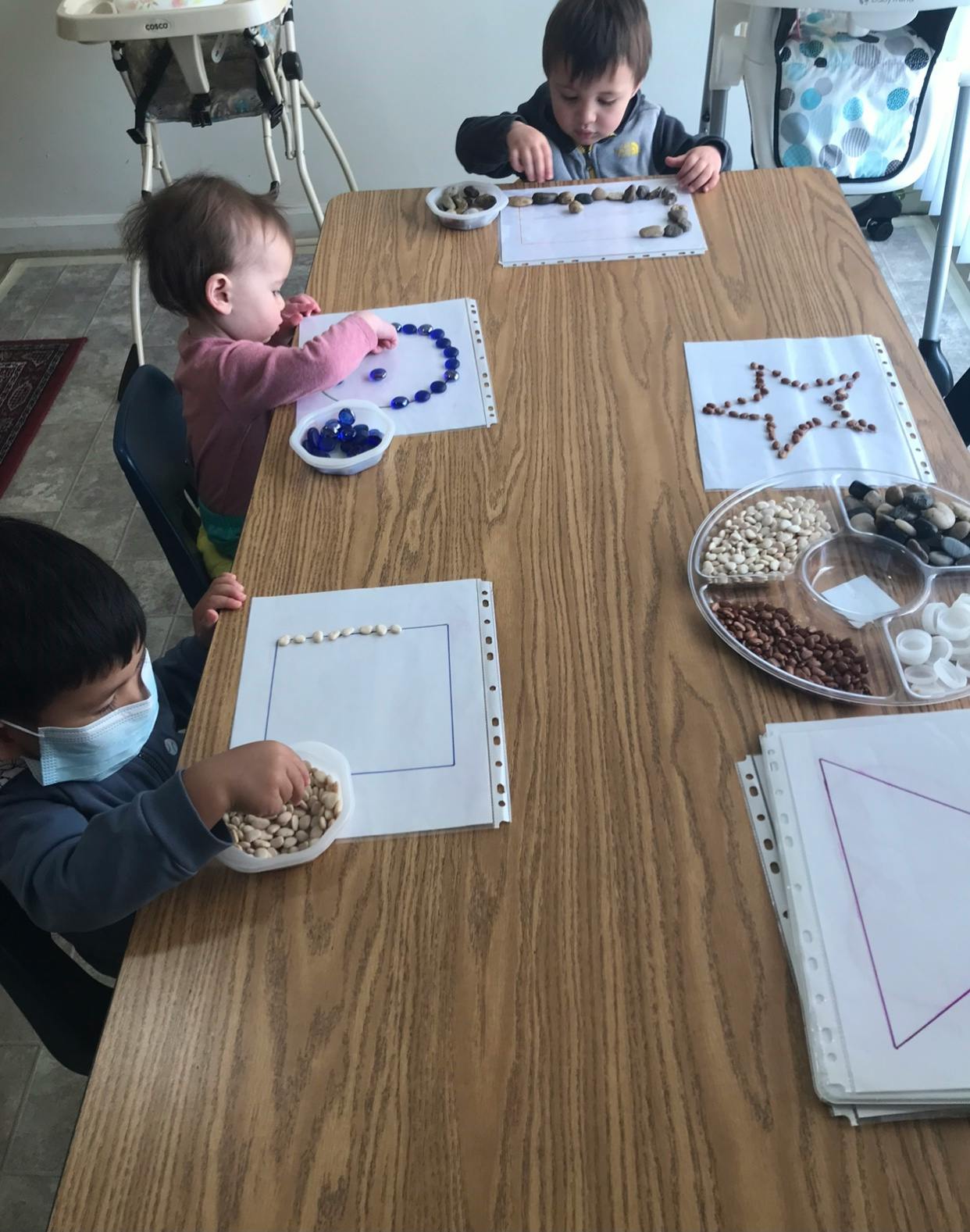 Three children at a table doing crafts with beads and pebbles