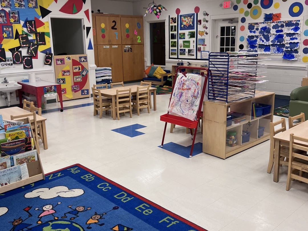 Classroom with small tables, an easel with a painting, and a drying rack