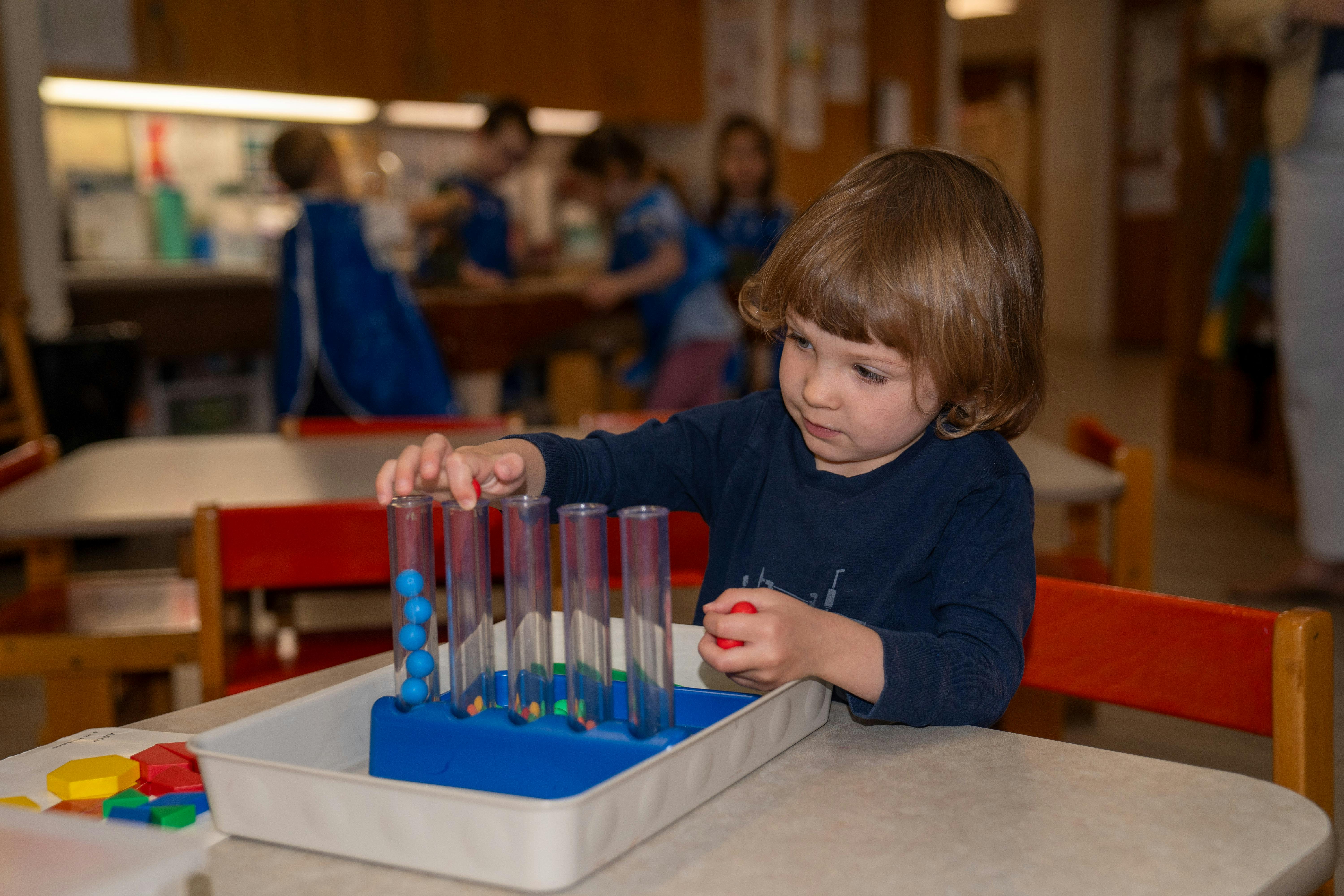 Child playing with a sorting toy at a table in a classroom
