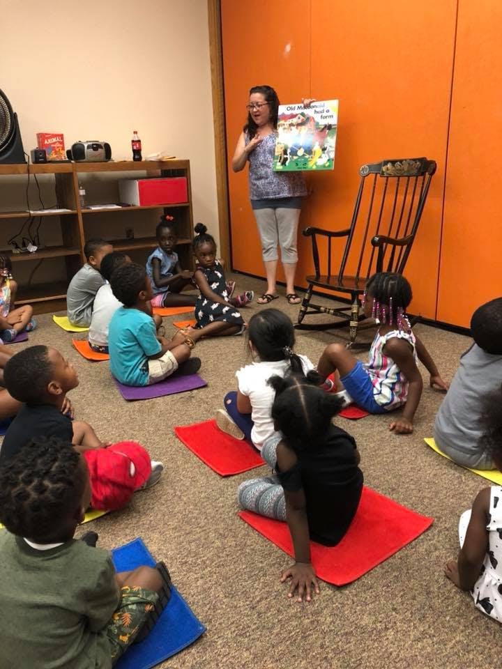 Adult holding a book and speaking to a group of children sitting on the floor