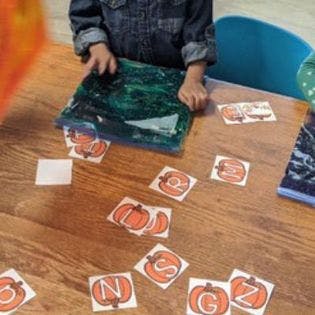 Child playing with sensory bag and alphabet cards on a table