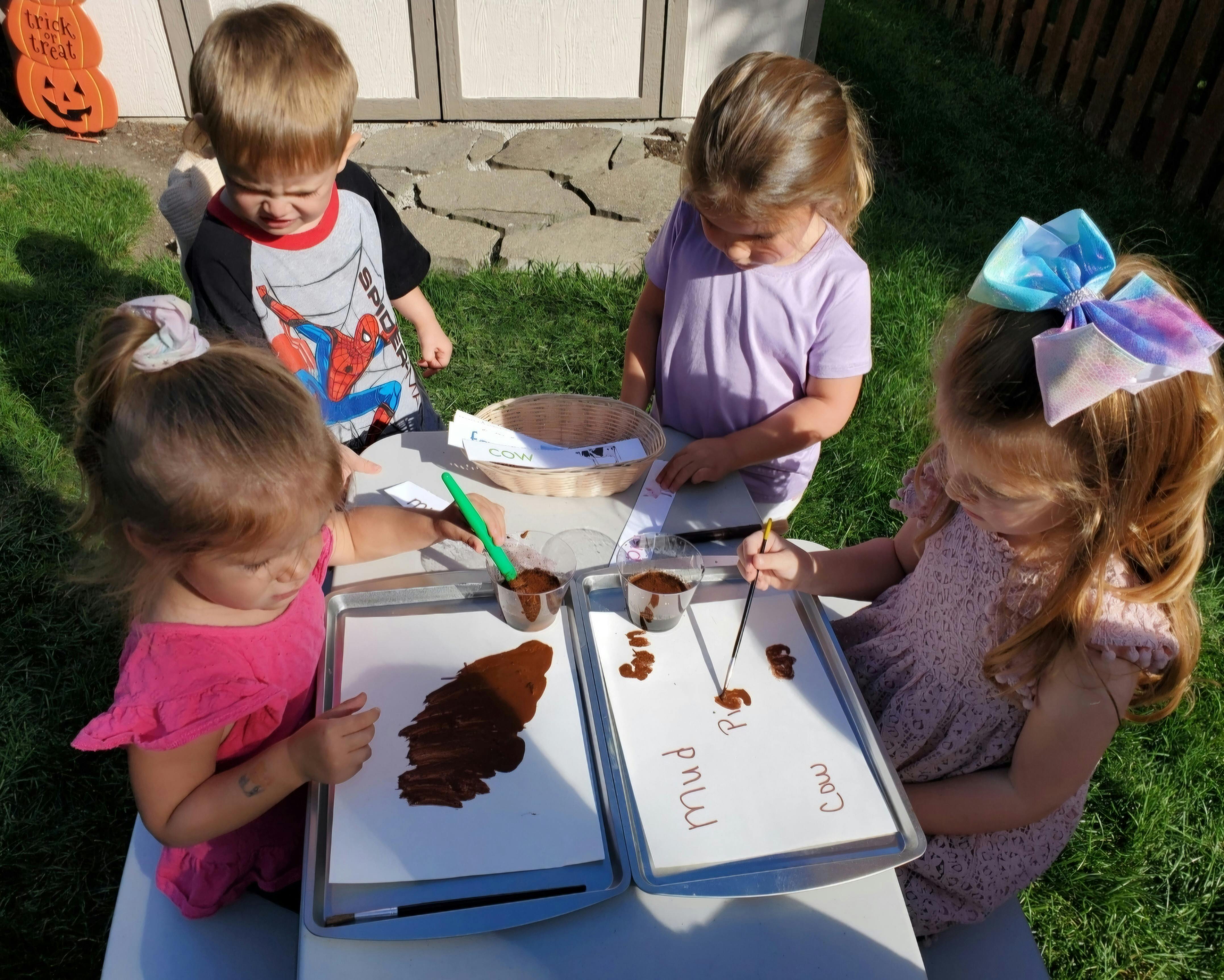 Four children painting with mud on trays outdoors