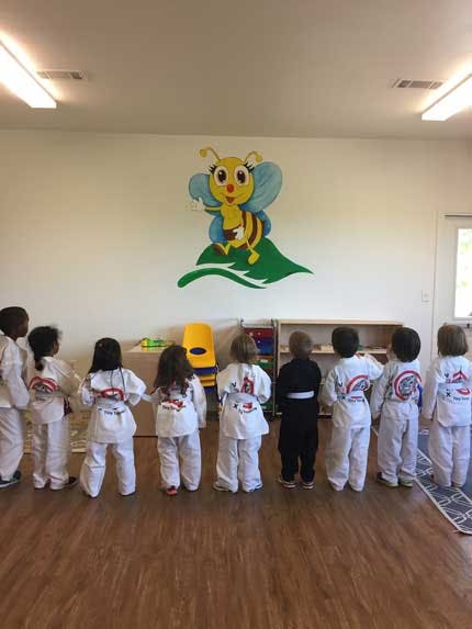 Children in martial arts uniforms standing in a line facing a wall mural