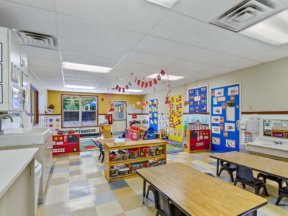 Colorful preschool classroom with tables, chairs, and play areas