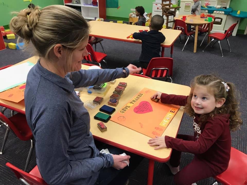 Adult and child stamping on paper at a table in a classroom