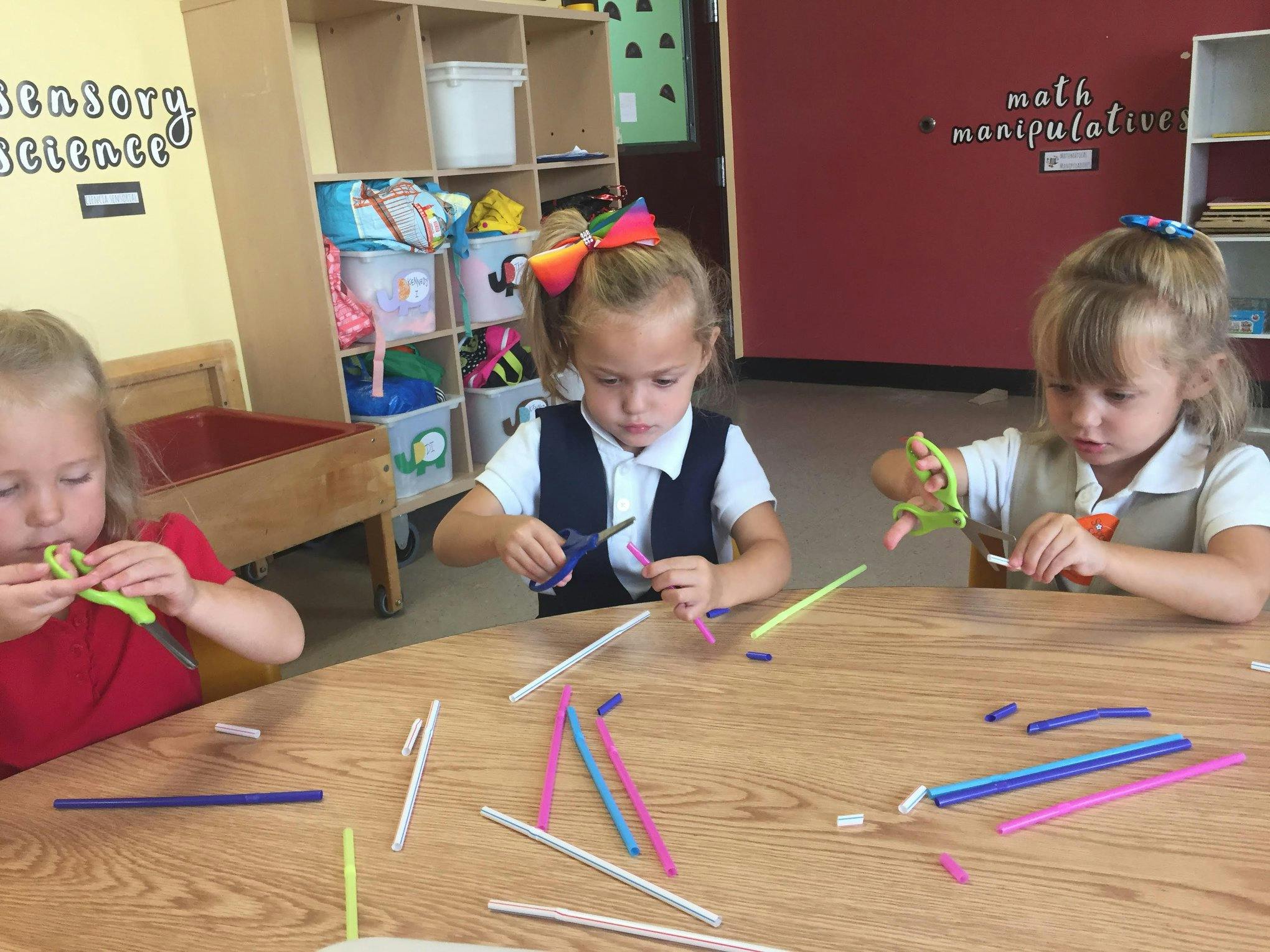 Three children cutting pipe cleaners at a table