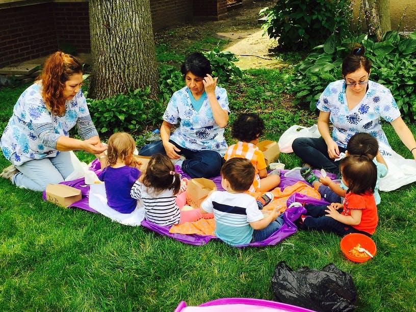 Three people and several children sitting on blankets on grass