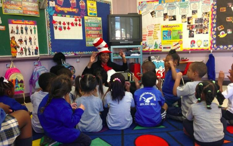 Person in striped hat reading to children in a classroom