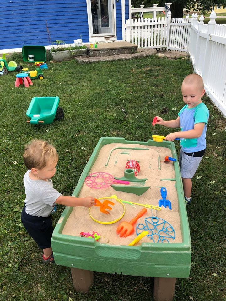 Two children playing with sand and toys in a sand table outdoors