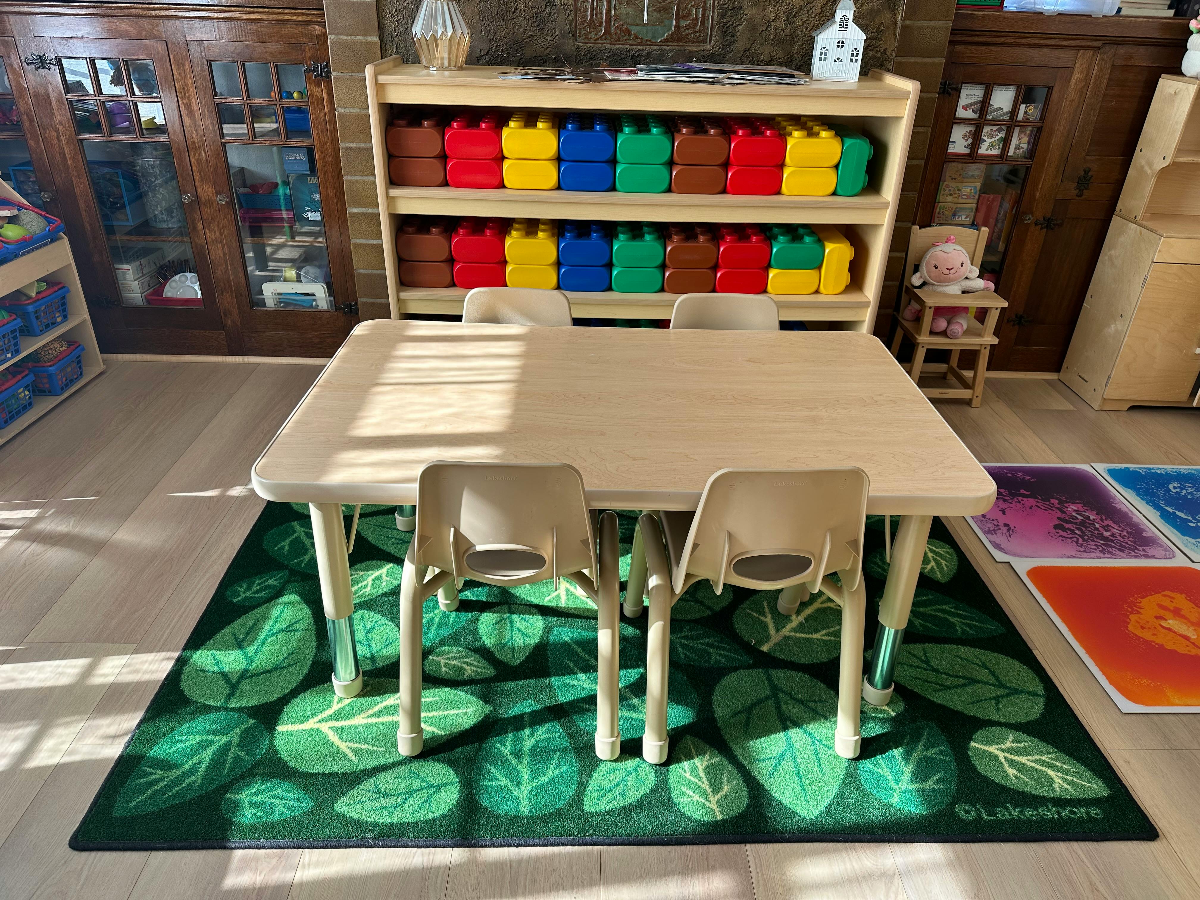 Table and chairs on a green leaf-patterned rug in a classroom