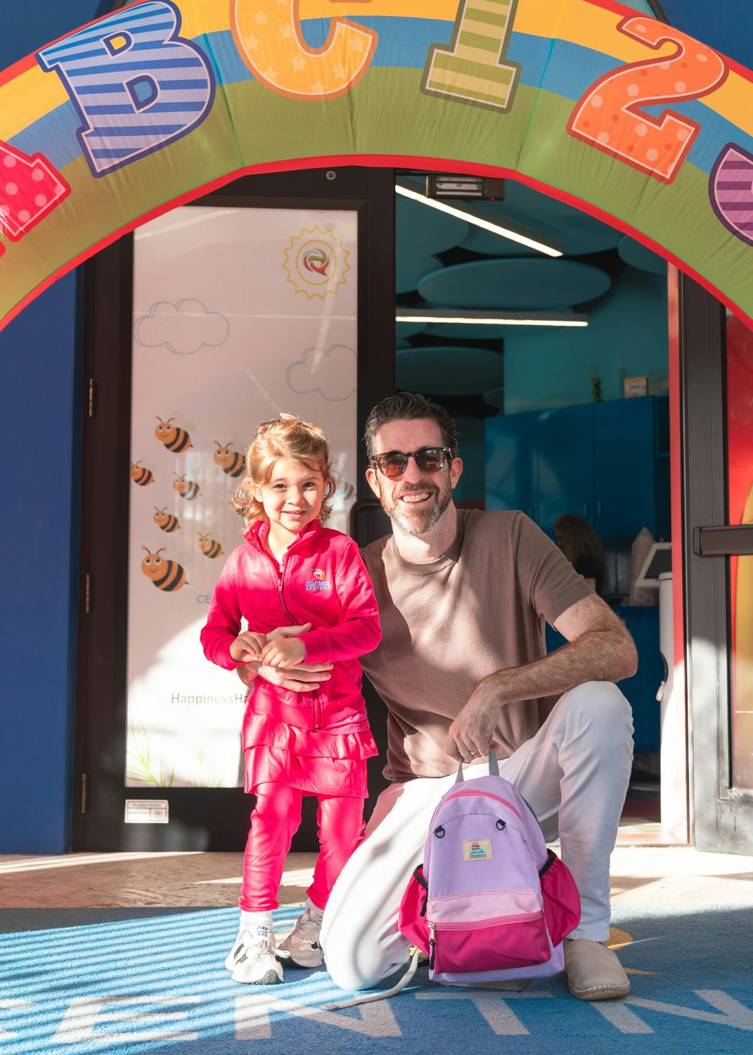 Adult and child standing under a colorful archway with a backpack