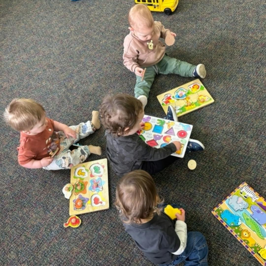 Four children playing with puzzles on a carpeted floor