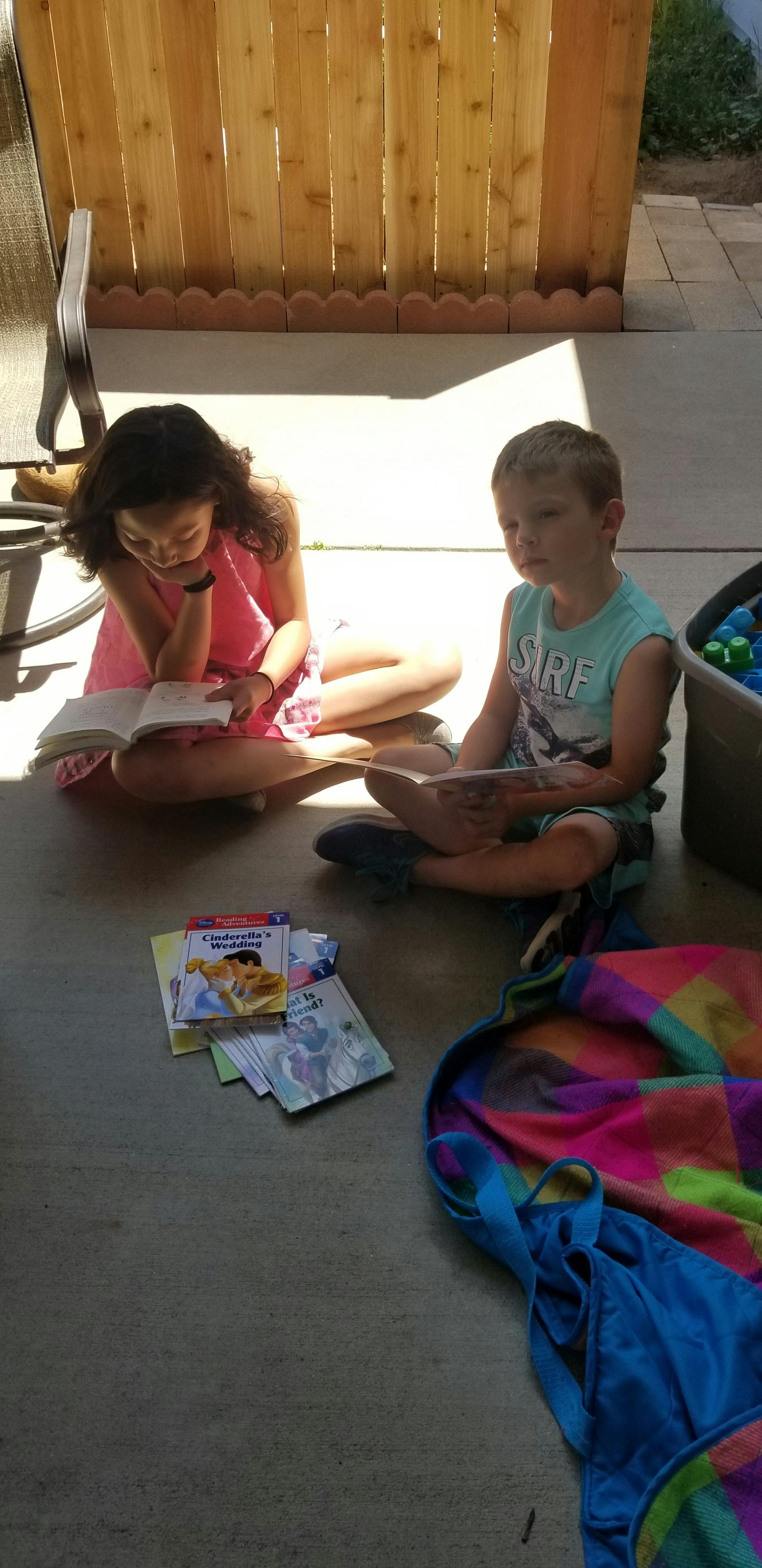 Two children sitting on the ground reading books