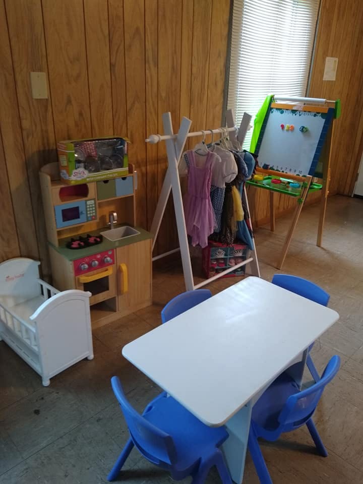 Children's play area with toy kitchen, clothes rack, easel, and table with chairs