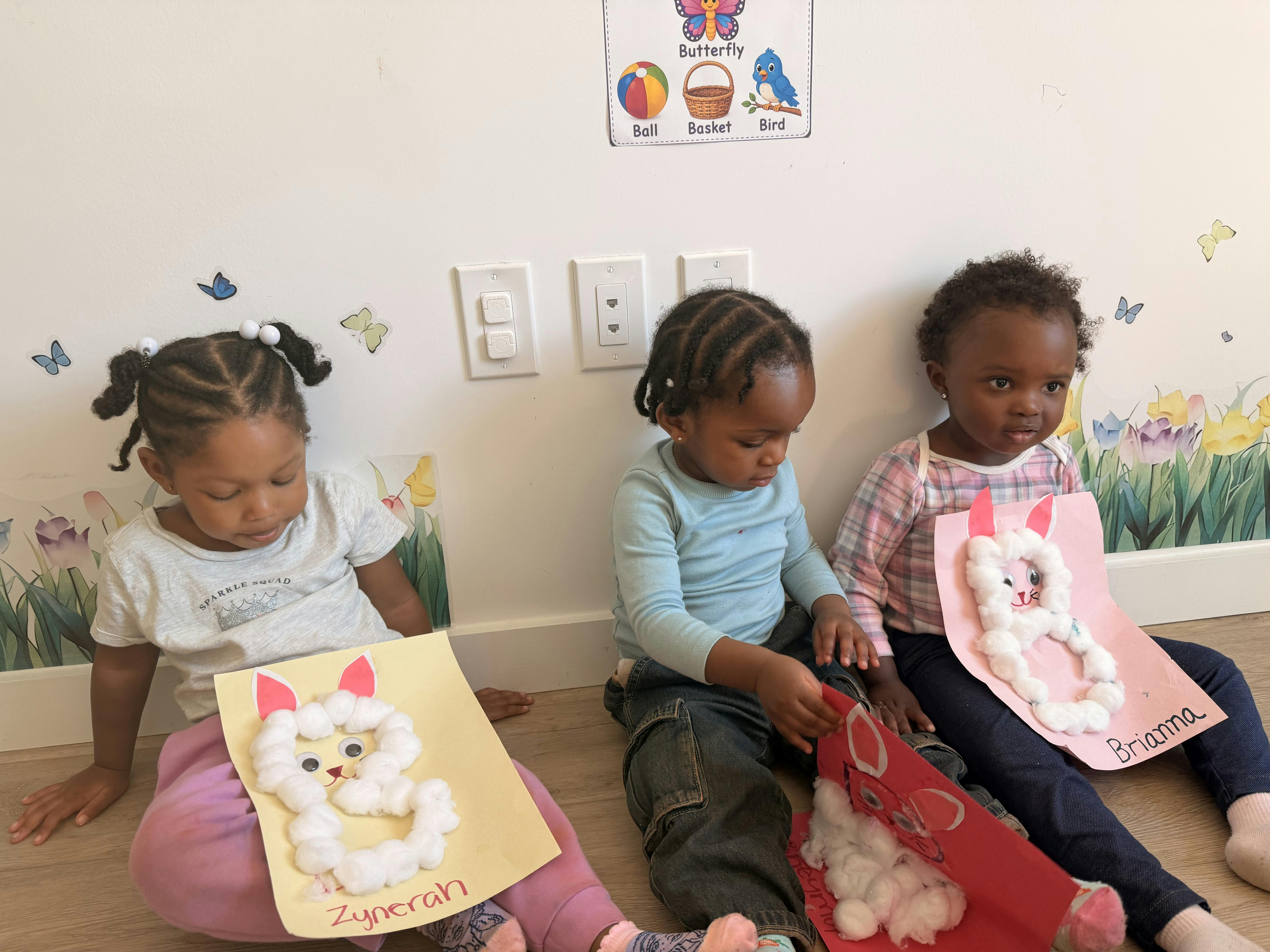 Three children sitting on the floor making cotton ball rabbit crafts