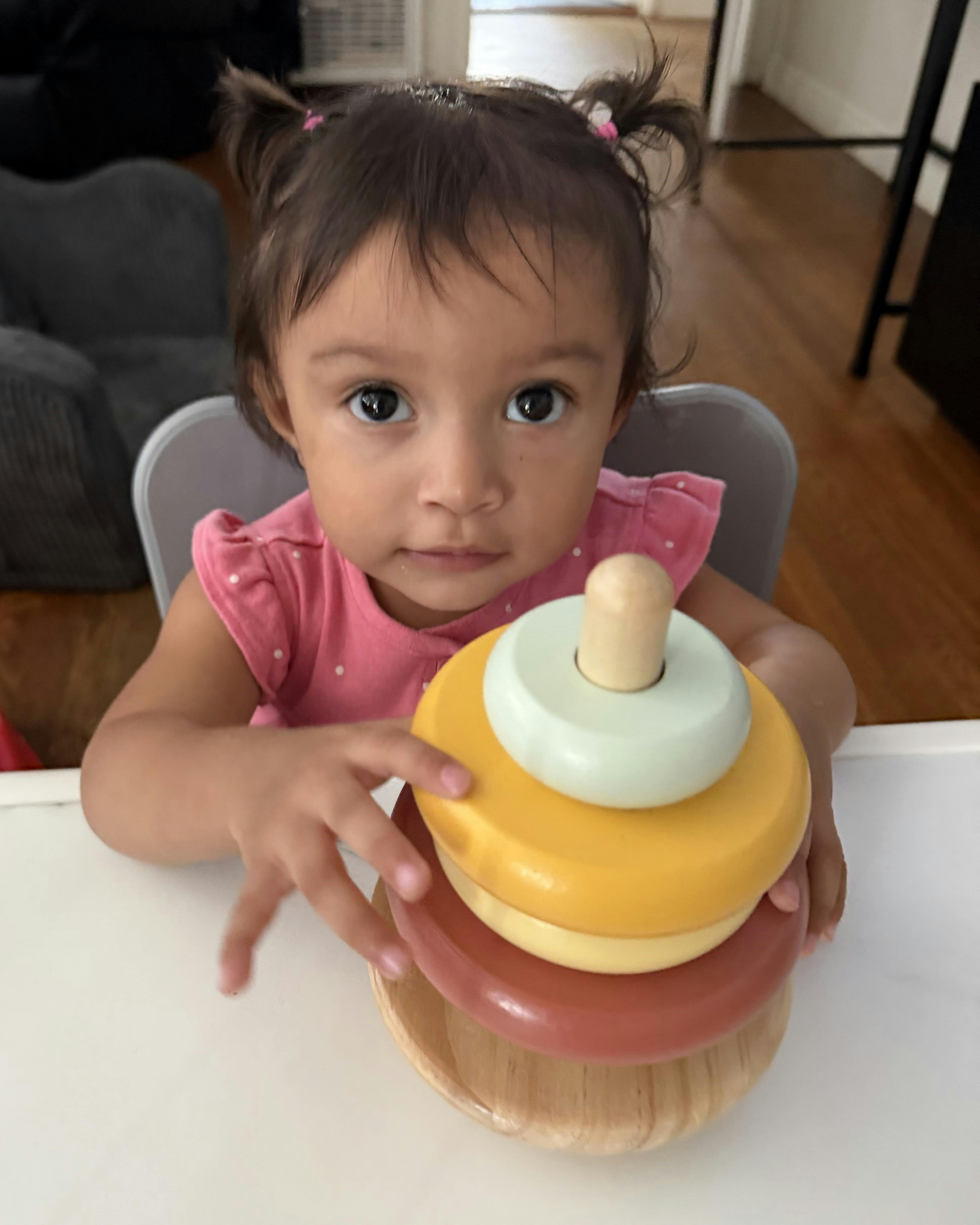 Child sitting in a high chair playing with a wooden stacking toy
