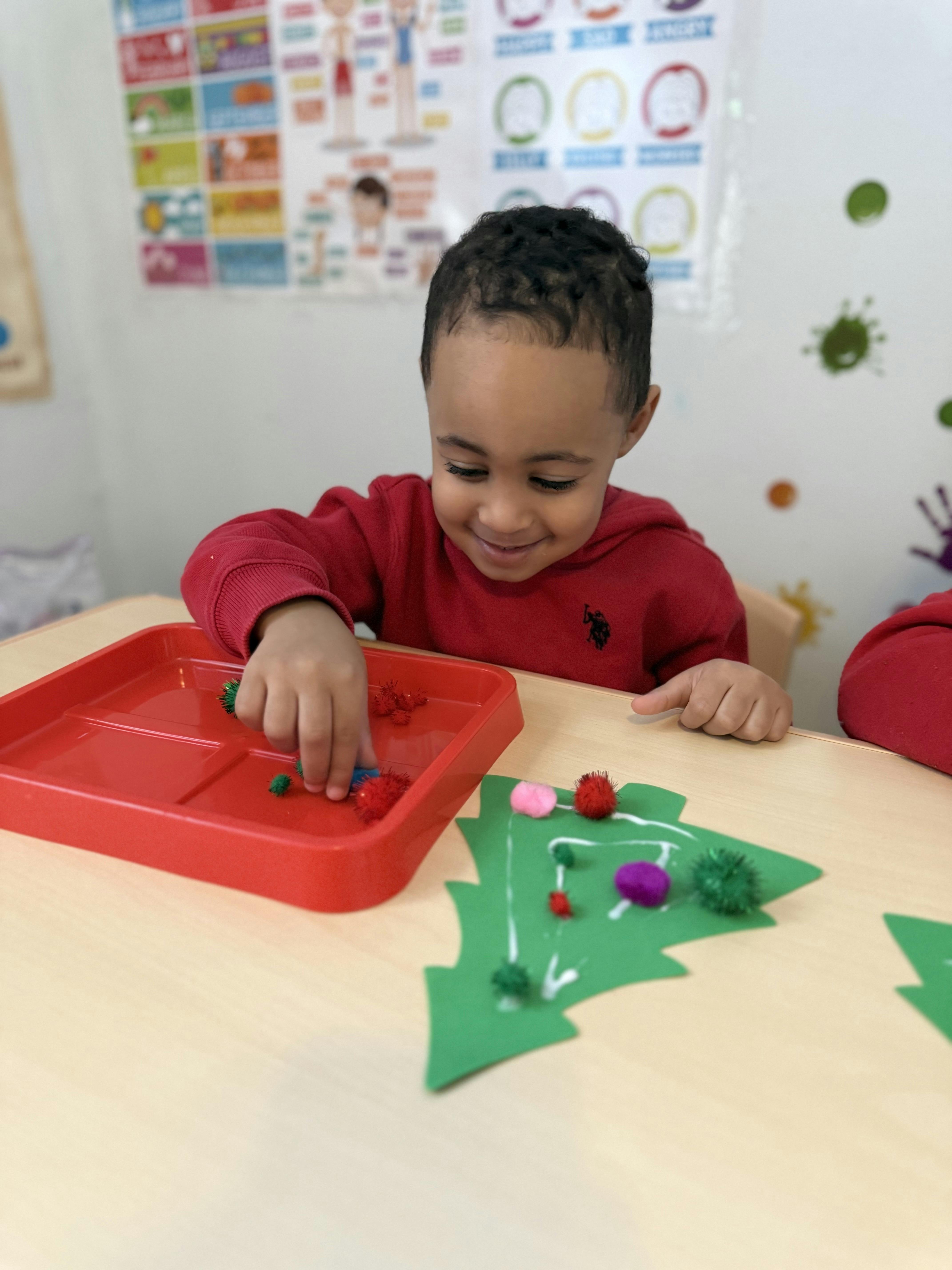 Child crafting with colorful pom-poms and a green paper Christmas tree