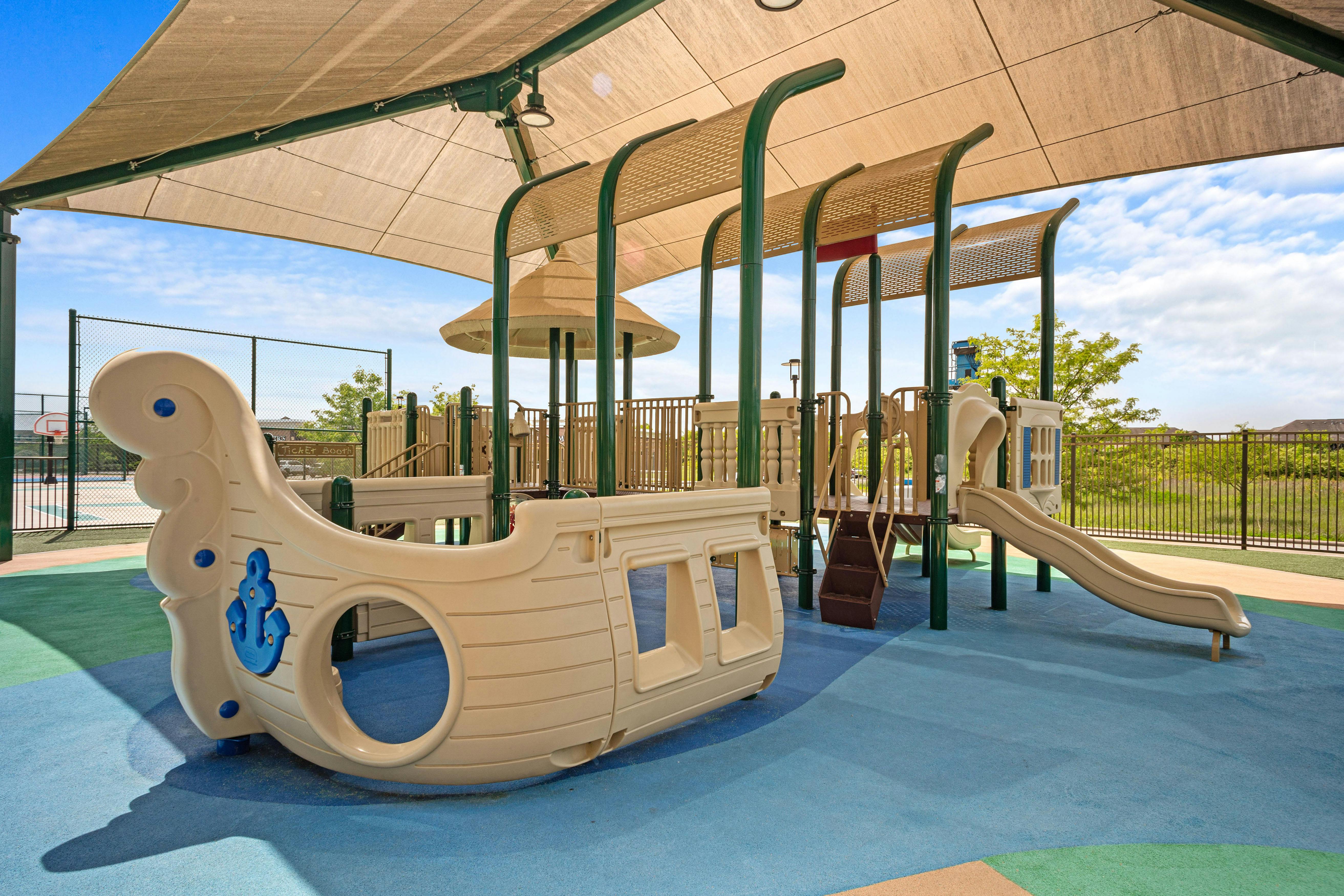 Playground with shaded play structure, slide, and a boat-shaped climber