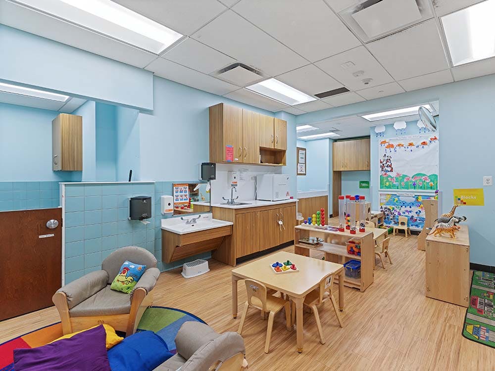 A playroom with small tables and chairs, a sink area, and toys