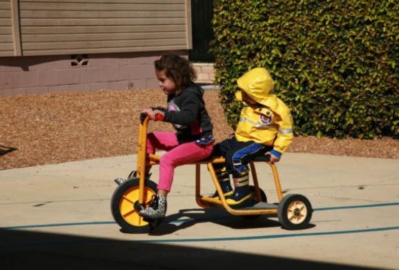 Two children riding a yellow tricycle together