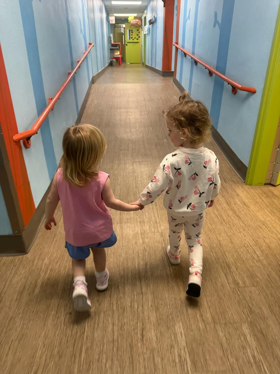 Two children holding hands and walking down a hallway