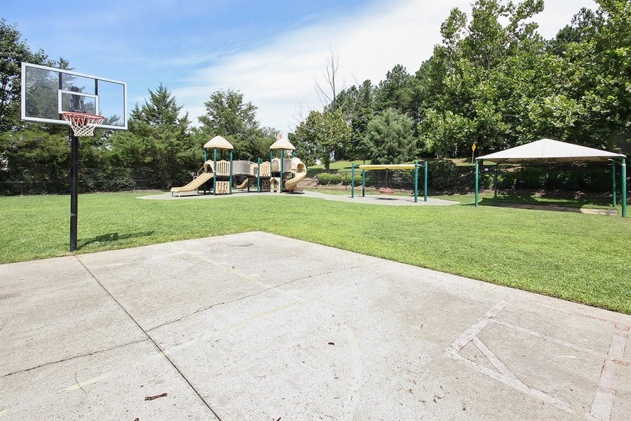 Basketball hoop and court with a playground and covered picnic area in background