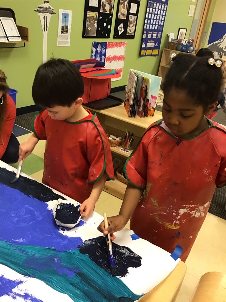 Two children in smocks painting on a large sheet of paper