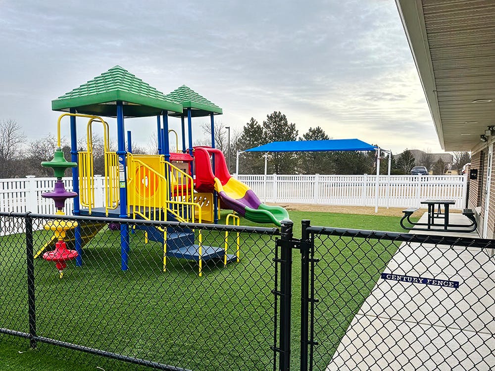 Colorful playground structure on artificial turf with a fence and building