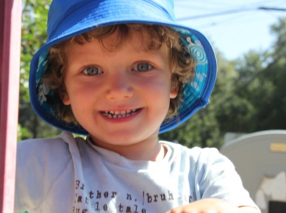 Child with curly hair wearing a blue hat and smiling