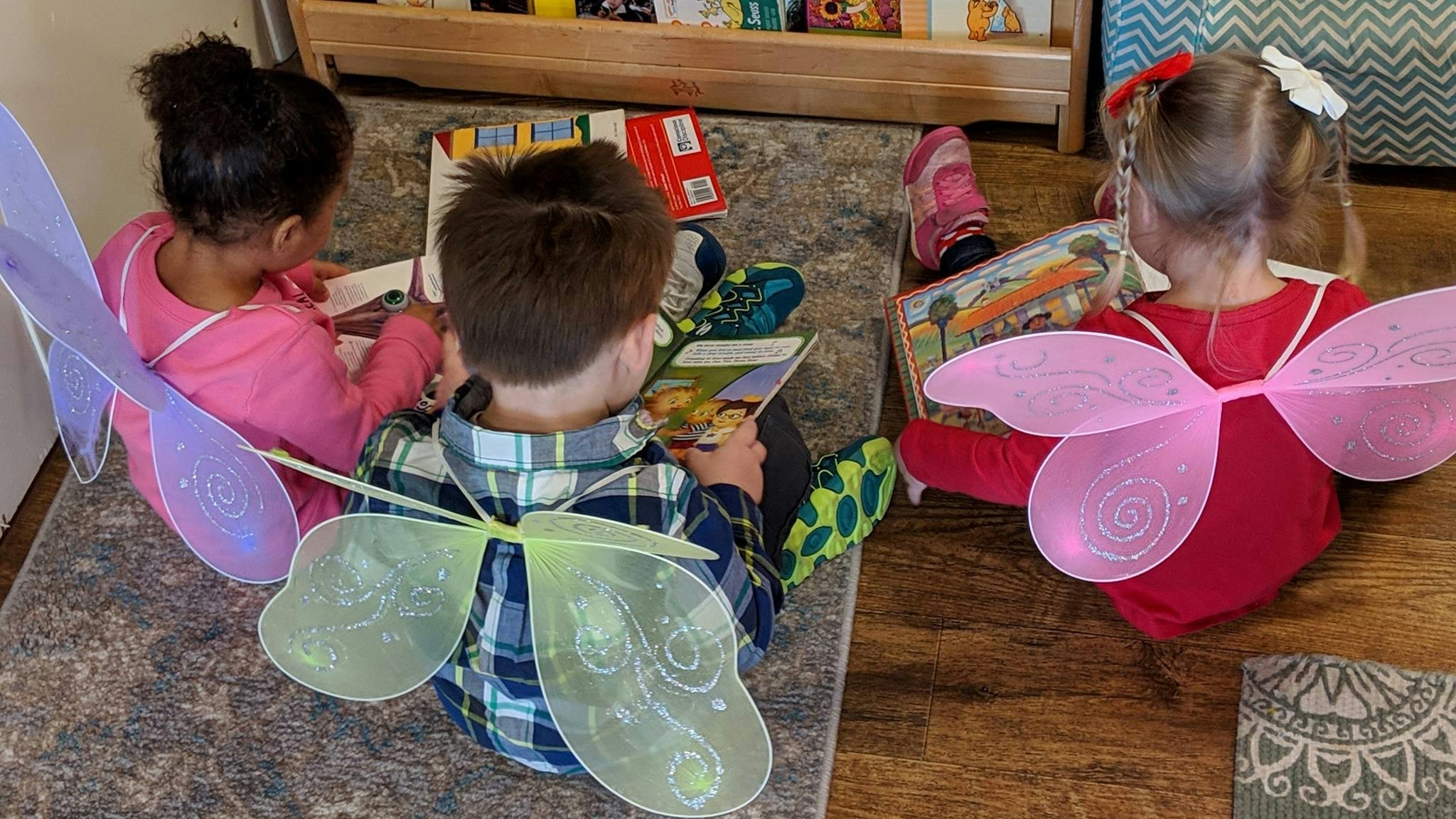 Three children wearing fairy wings reading books