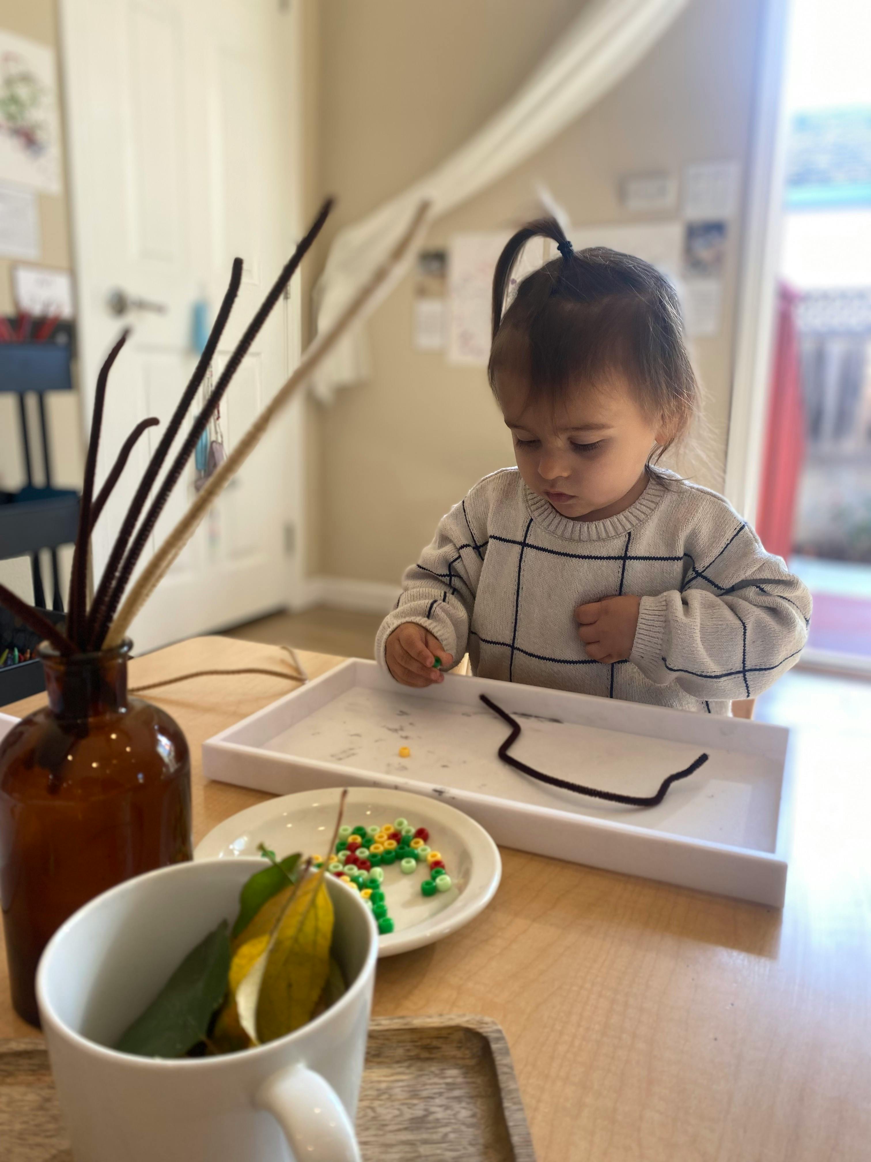 Child playing with small colorful beads on a white tray