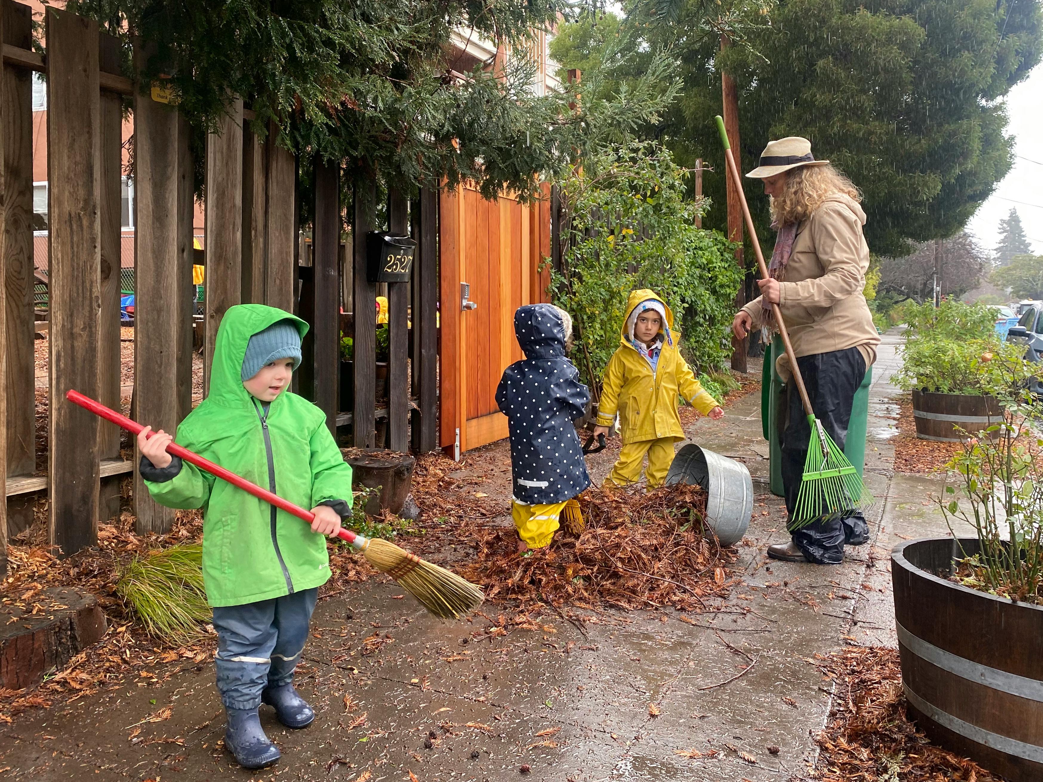 Adult and three children raking leaves on a paved path