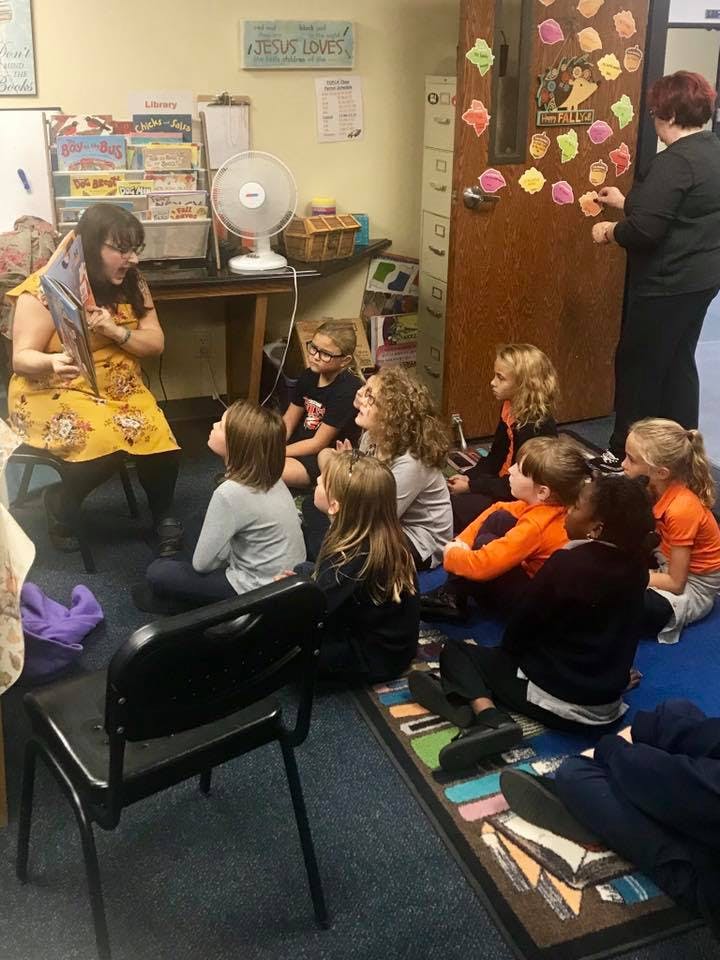Person reading to a group of children sitting on the floor