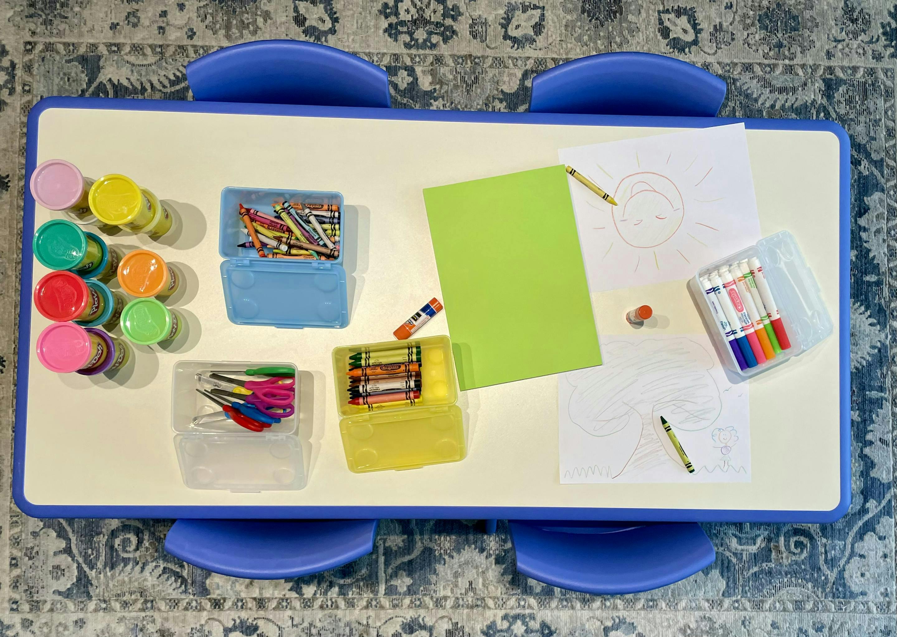 Art supplies on a table with paper, crayons, markers, and paint pots