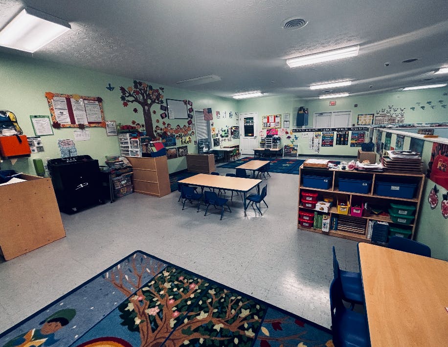 Empty preschool classroom with tables, chairs, and learning stations
