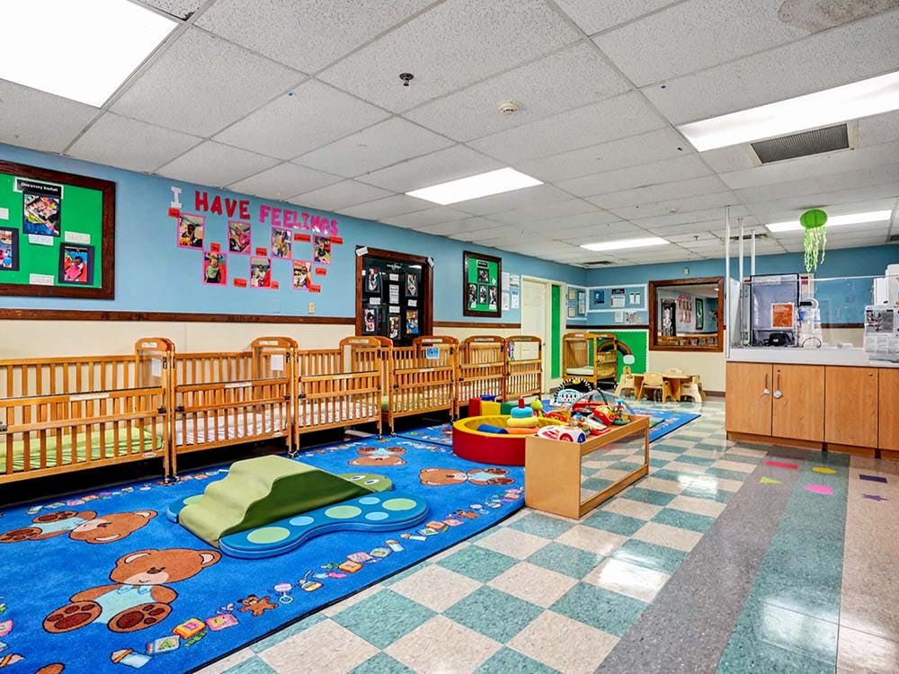 Cribs in a daycare room with a play mat, toys, and \