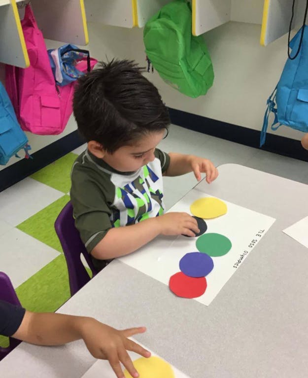 Child playing with colorful paper circles on a table in a classroom