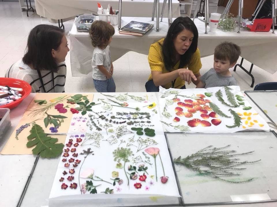 Adult and two children looking at pressed flowers and leaves on a table