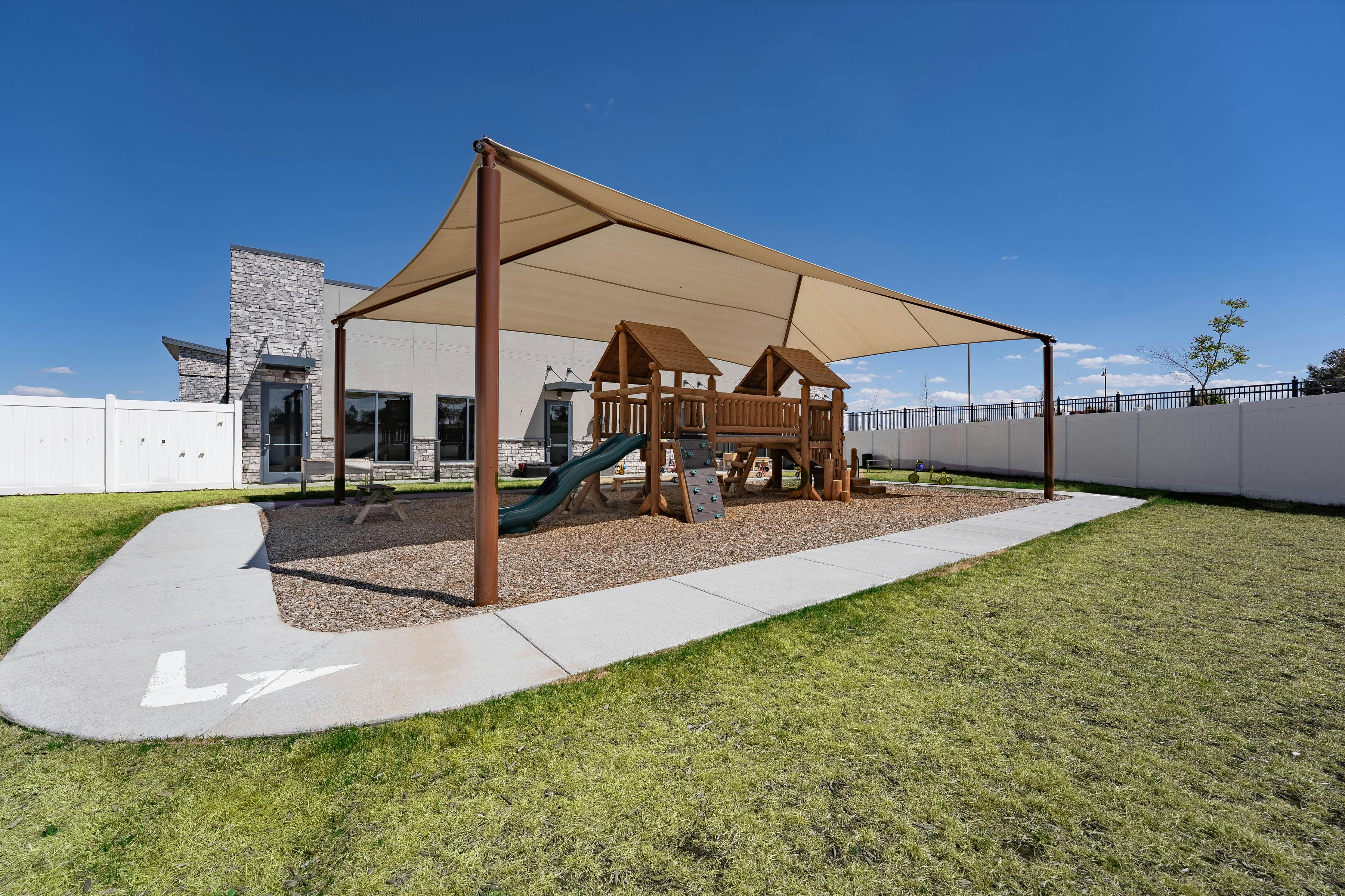 Playground with wooden play structure and green slide under a shade cover
