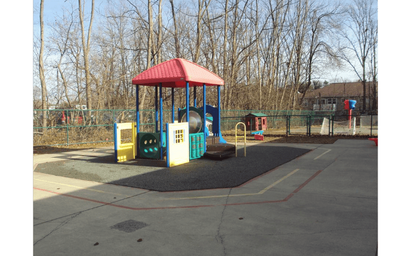 Colorful playground structure on a paved area with trees in the background