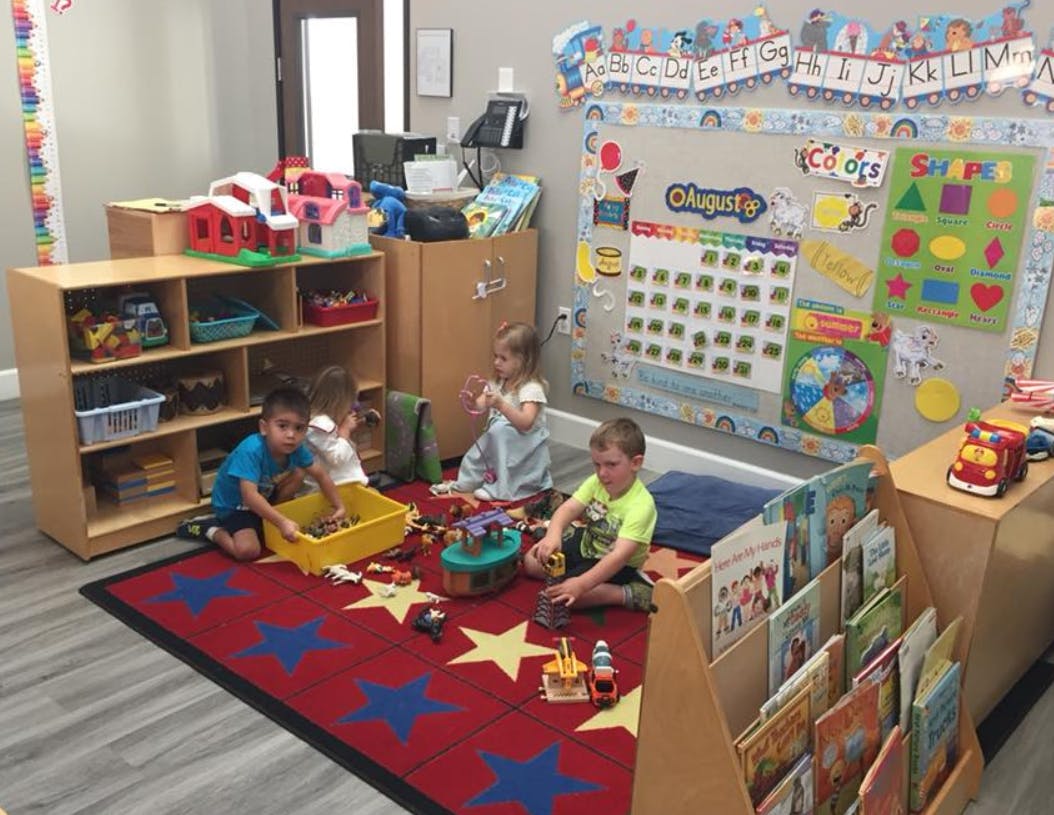 Three children playing with toys on a rug in a classroom