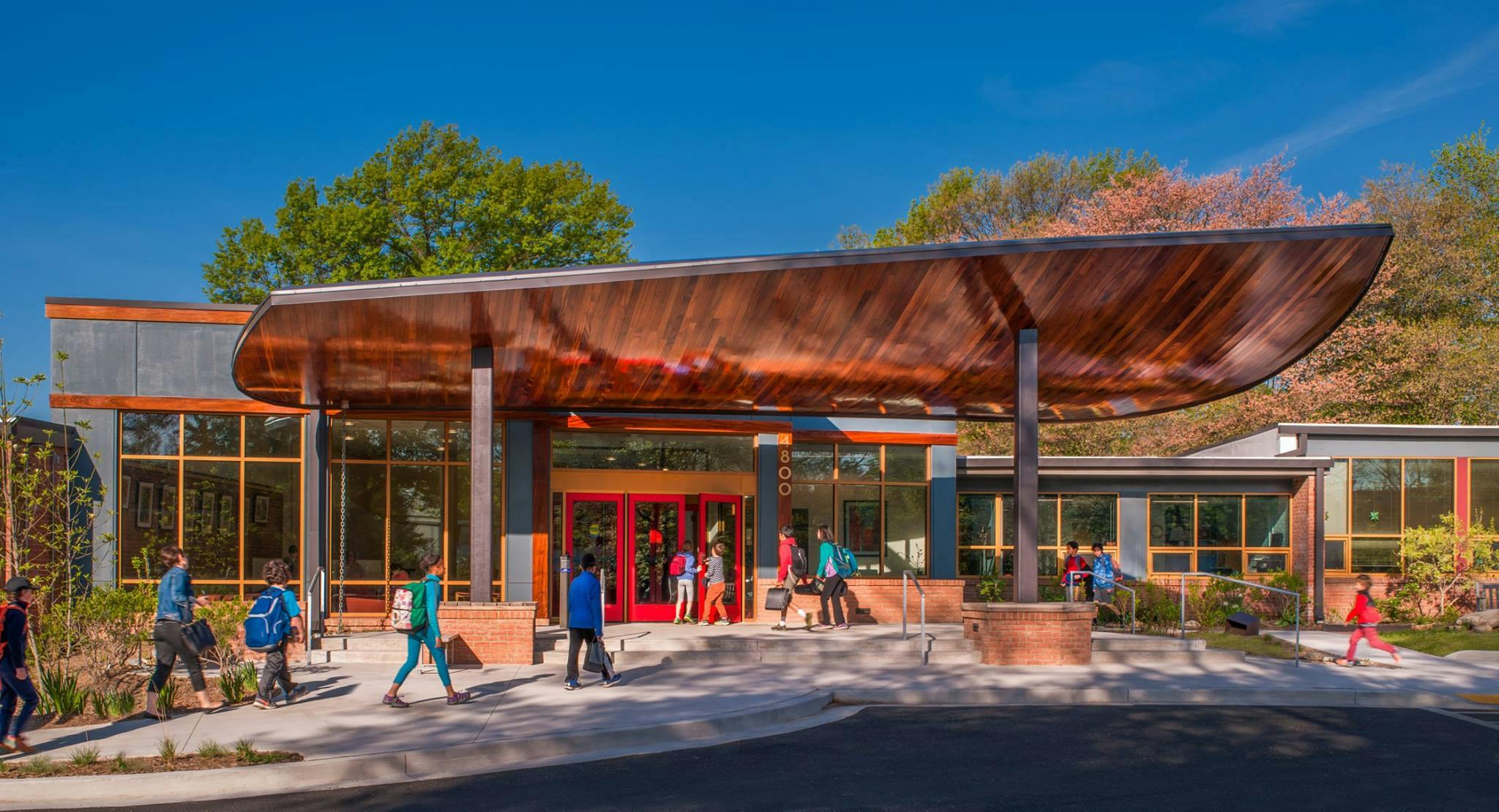 People walking outside a building with a large, curved wooden canopy