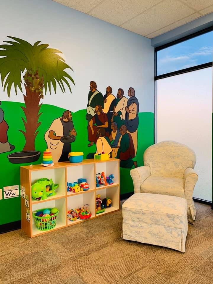 Wall mural of people under a palm tree, toy shelf, and armchair with ottoman