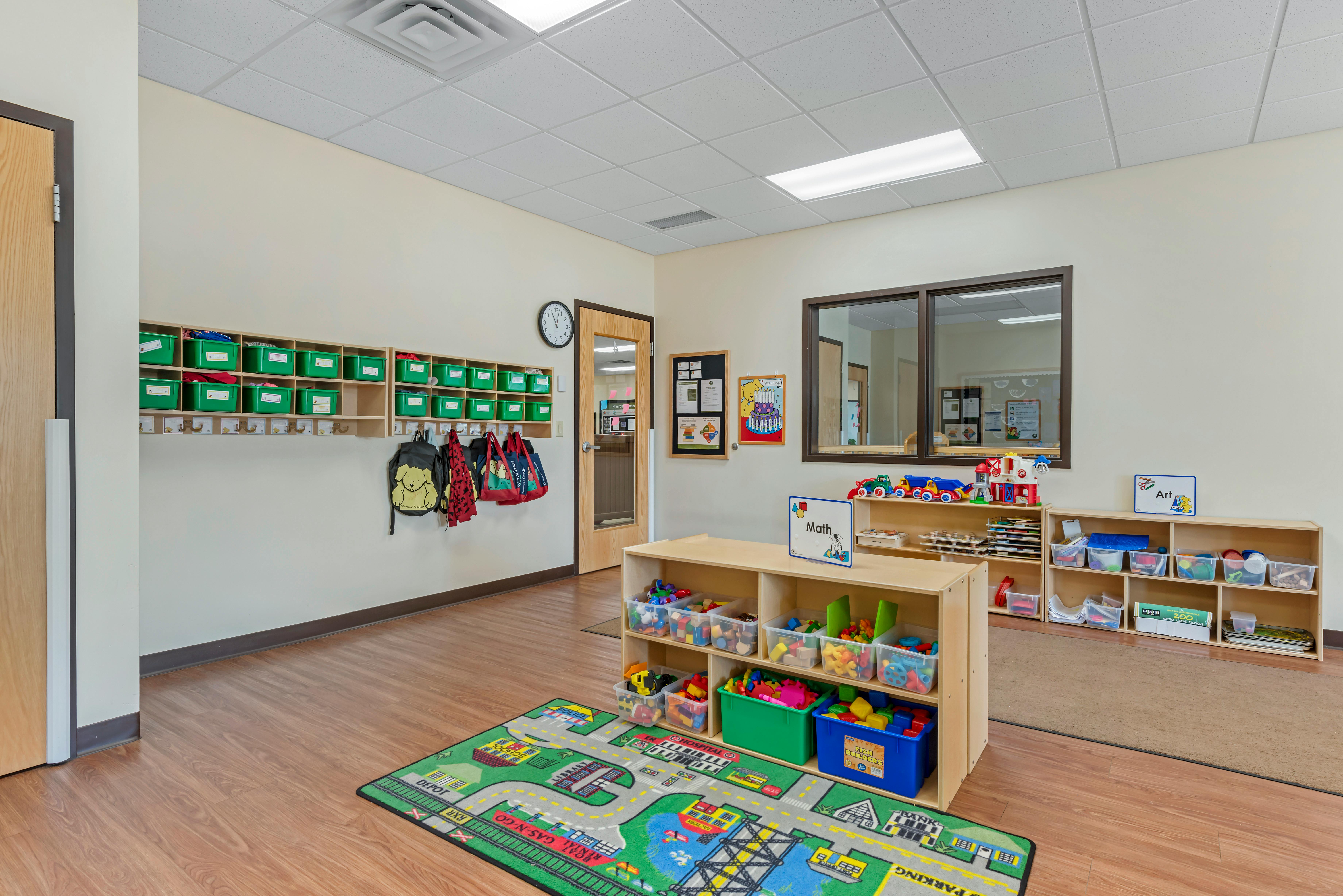 Classroom with cubbies, backpacks on hooks, toy shelves, and a road map play rug